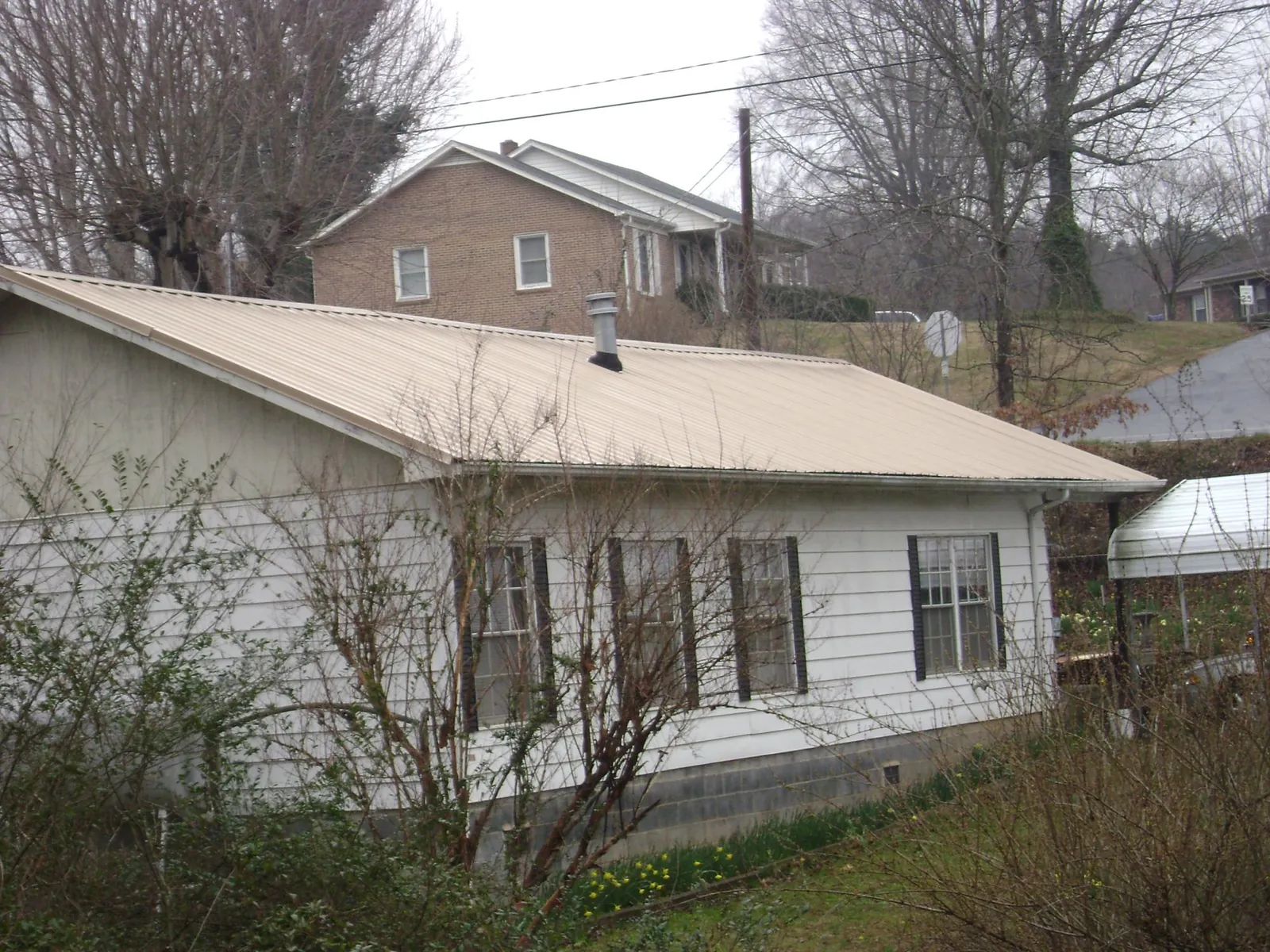 Tan metal roof on a white sided house set into a hillside — Commercial Roofing by Roofing Brothers in Clare